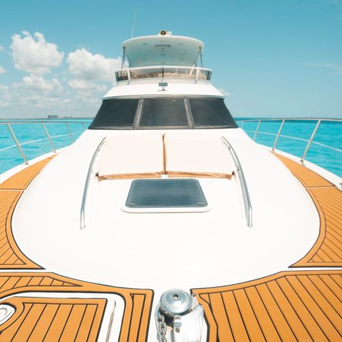Yacht bow with teak deck, sun pads, and anchor over turquoise water.
