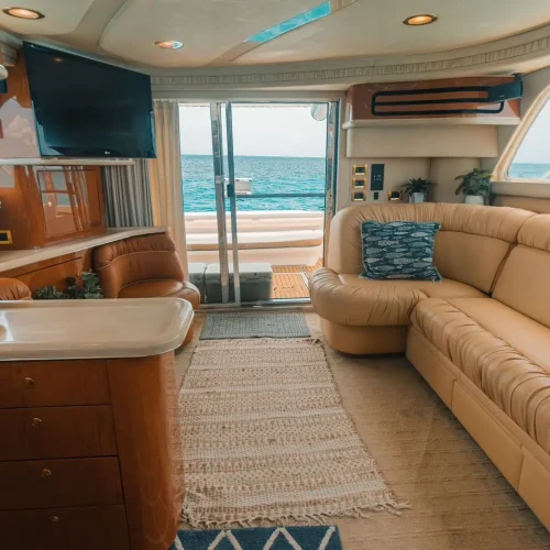 Yacht salon with tan leather sofa, TV, and sliding doors to ocean deck.
