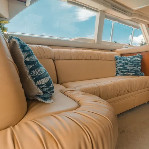 Curved tan leather sofa with fish-print pillows below yacht windows.