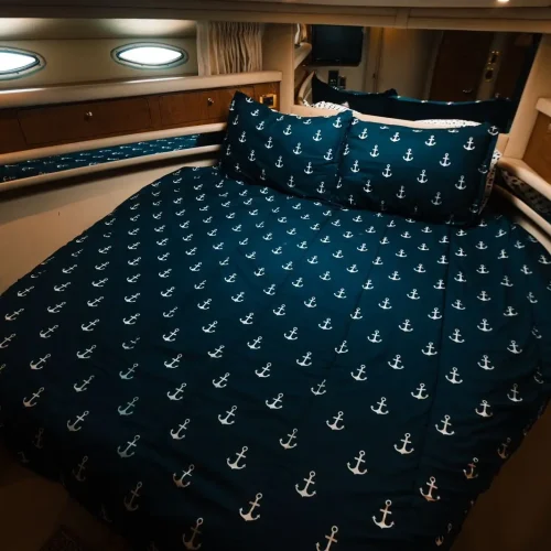 Yacht cabin bed with navy anchor-print bedding and porthole windows.