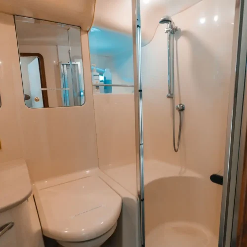 Compact yacht bathroom with toilet, mirror, and glass shower enclosure.
