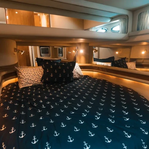 V-berth cabin bed with navy anchor bedding and warm cabin lighting.