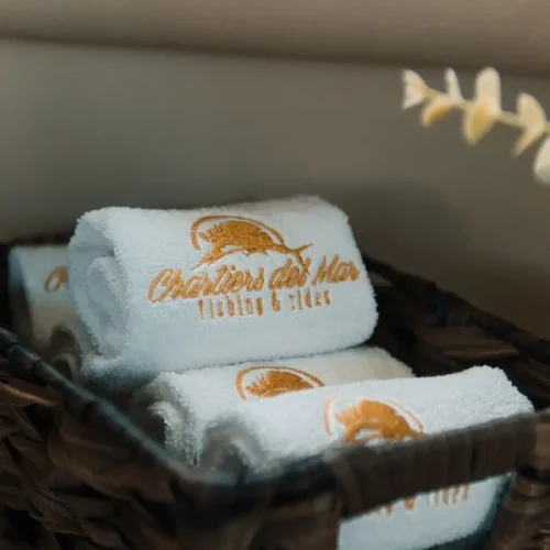 Rolled towels with gold logo displayed in woven basket aboard yacht.