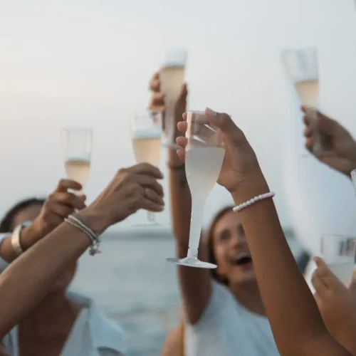 Guests raising champagne glasses for a toast during a sunset yacht party.