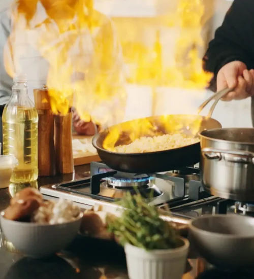 Cooking, pan and hands of man with fire in house kitchen for diet, private service and nutrition. People, recipe and personal chef frying food with flame for gourmet cuisine, hospitality or lunch